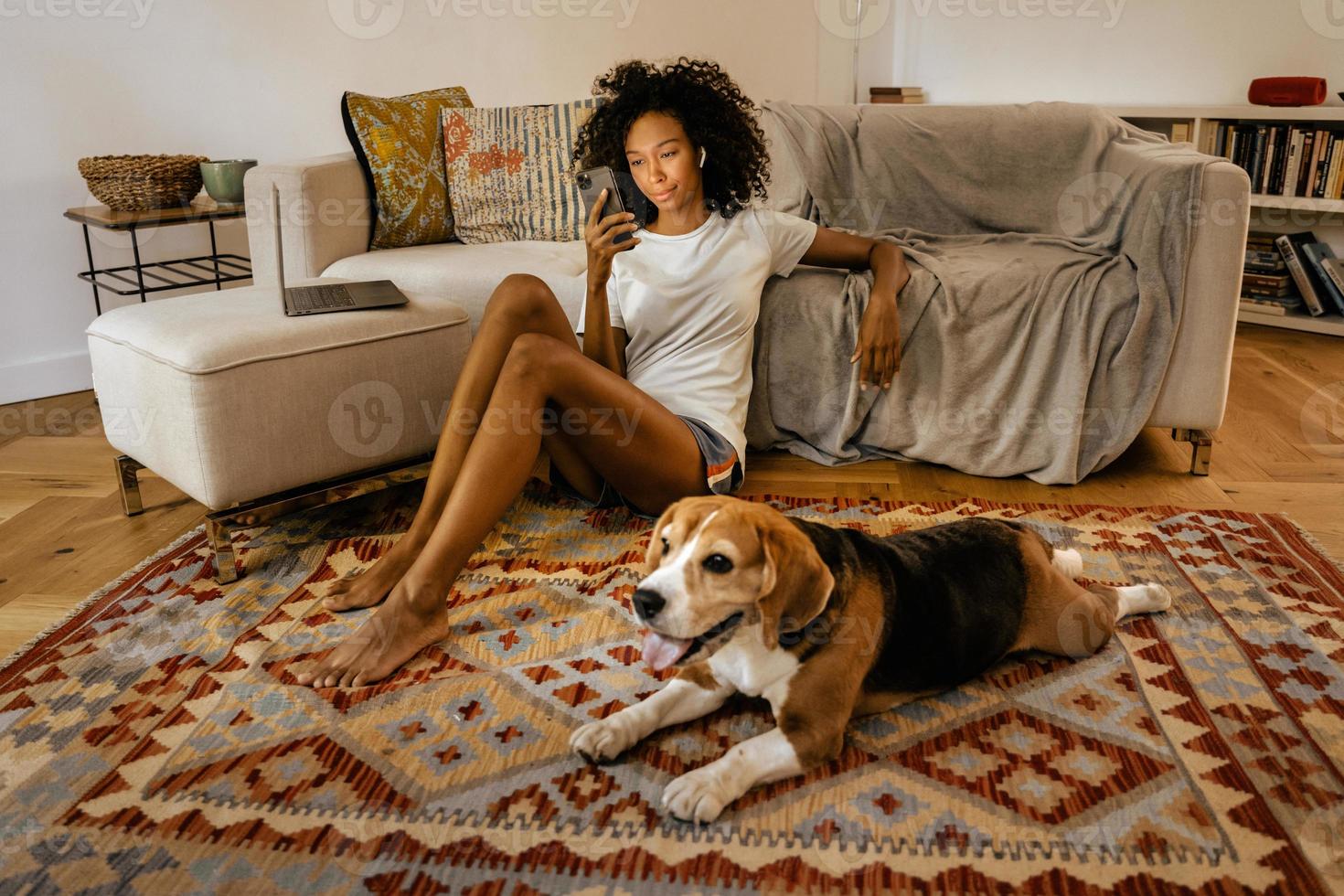 Schwarze Frau mit Handy, während sie mit ihrem Hund auf dem Boden sitzt foto