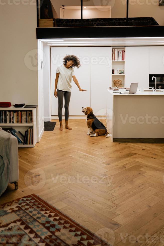 schwarze junge Frau lächelt beim Spielen mit ihrem Hund zu Hause foto