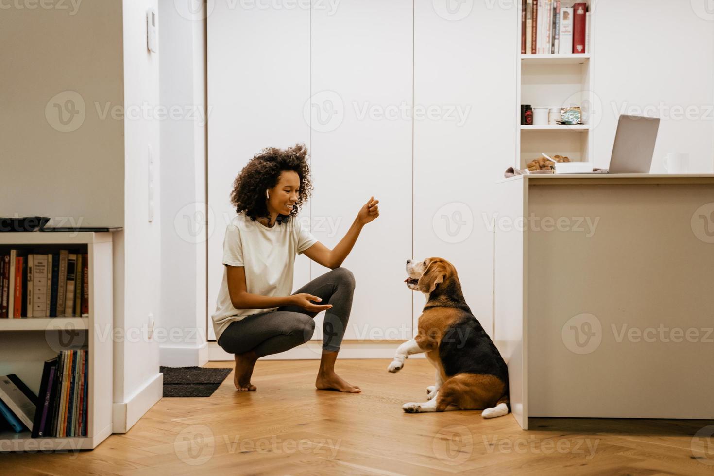 schwarze junge Frau lächelt beim Spielen mit ihrem Hund zu Hause foto