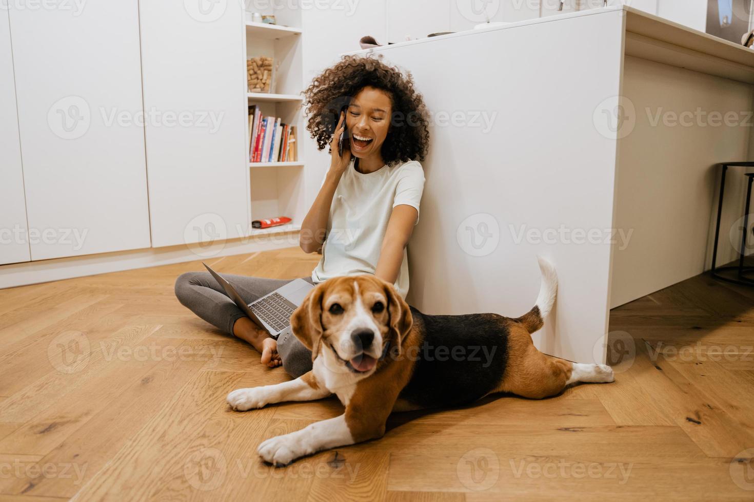 Schwarze junge Frau, die am Handy spricht und ihren Hund spielt foto