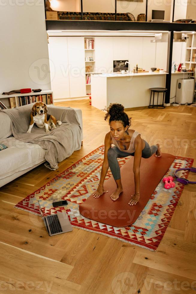 Schwarze junge Frau macht Salat, während sie Laptop in der Küche benutzt foto