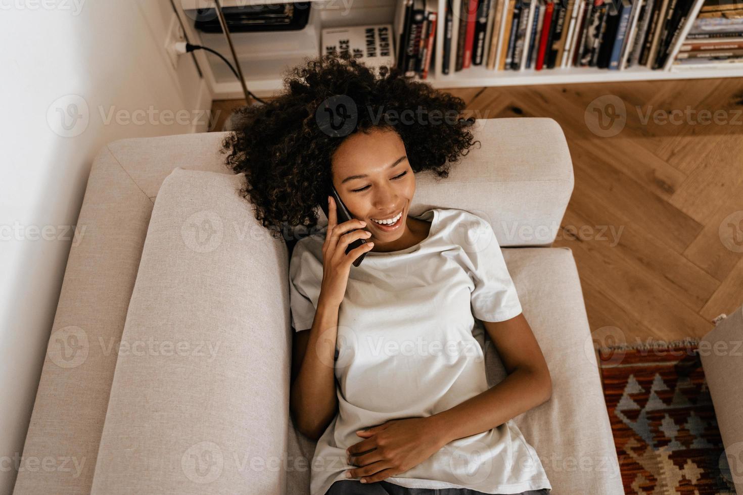 schwarze junge frau, die auf dem sofa telefoniert, während sie sich ausruht foto