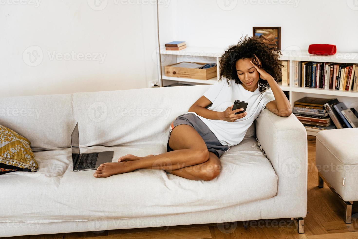 schwarze junge Frau mit Handy beim Ausruhen auf dem Sofa foto