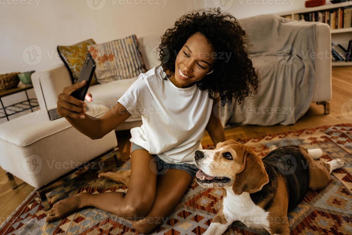 Schwarze Frau macht Selfie mit ihrem Hund, während sie auf dem Boden sitzt foto