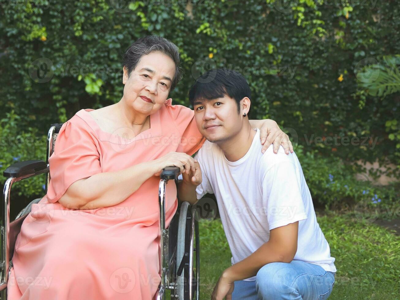 asiatisch Senior Frau Sitzung auf Rollstuhl mit ihr Sohn im das Garten. foto