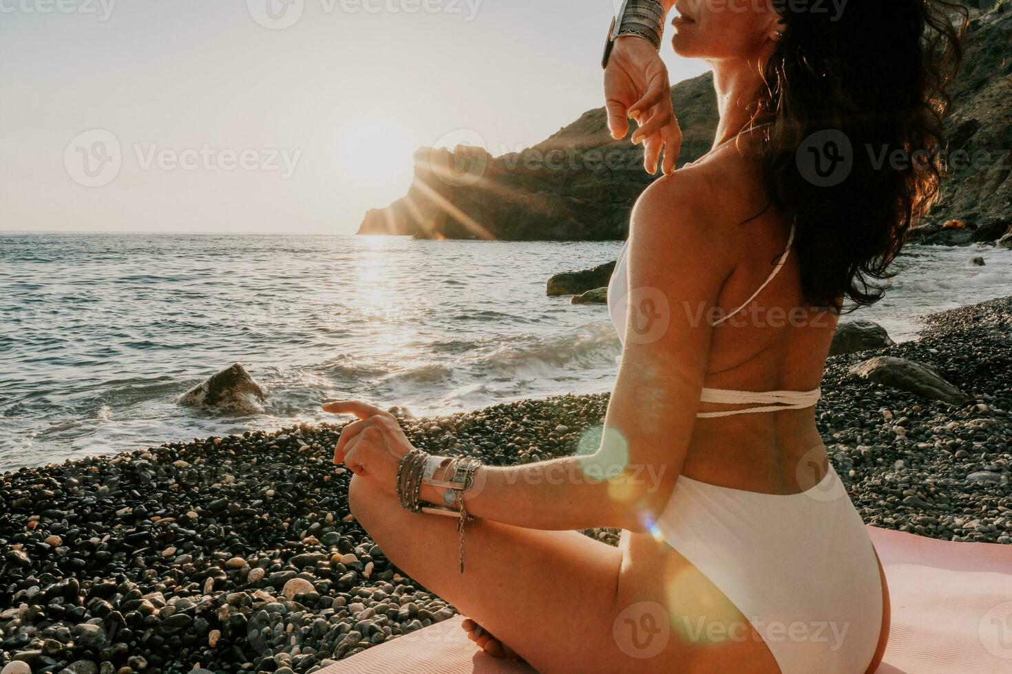 Frau Meer Yoga. glücklich Frau im Weiß Badeanzug und Boho Stil Armbänder üben draußen auf Yoga Matte durch Meer auf Sonnenuntergang. Frauen Yoga Fitness Routine. gesund Lebensstil, Harmonie und Meditation foto