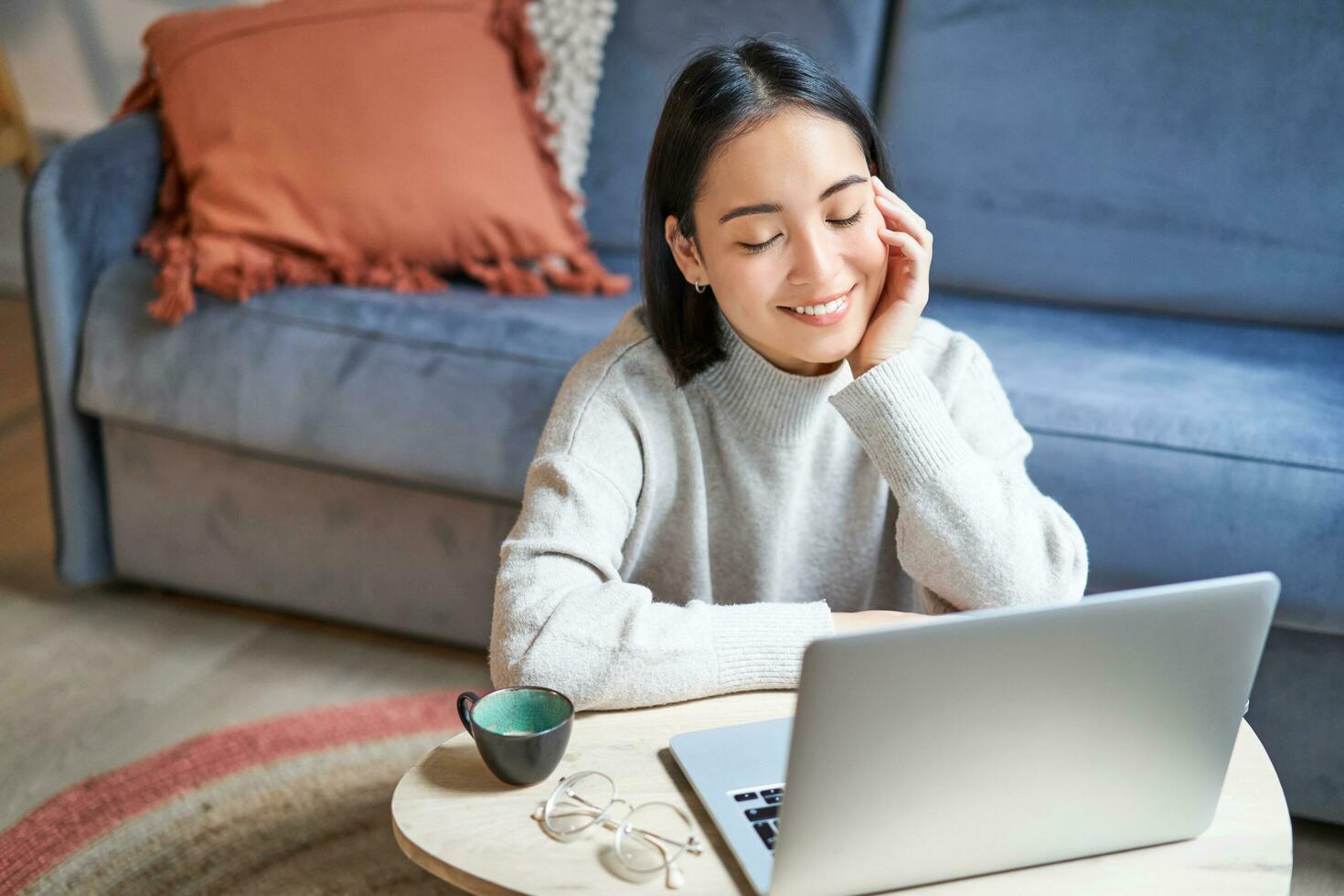 schön asiatisch Mädchen funktioniert von heim, studieren mit Laptop, Sitzung im Leben Zimmer, Sein auf Fernbedienung, freiberuflich tätig online foto