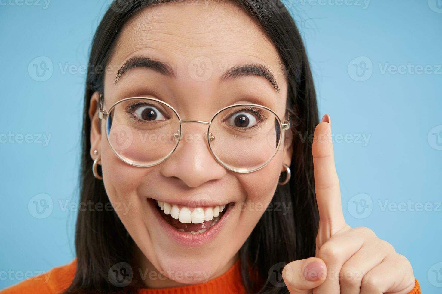 Eureka. schließen oben Porträt von aufgeregt Koreanisch Frau im Gläser, zeigt an einer Finger, hat ein Idee, steht Über Blau Hintergrund foto