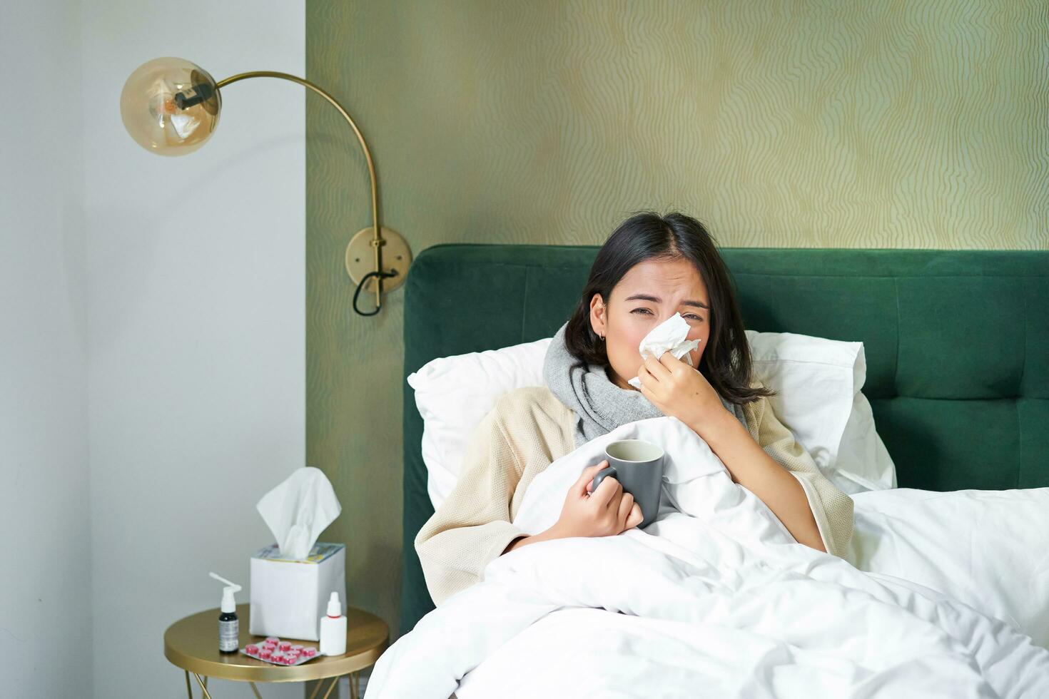 COVID-19, Grippe und Impfung Konzept. Koreanisch Mädchen Lügen im Bett mit kalt, fangen Grippe, Trinken heiß Tee und mit vorgeschrieben Medikation foto