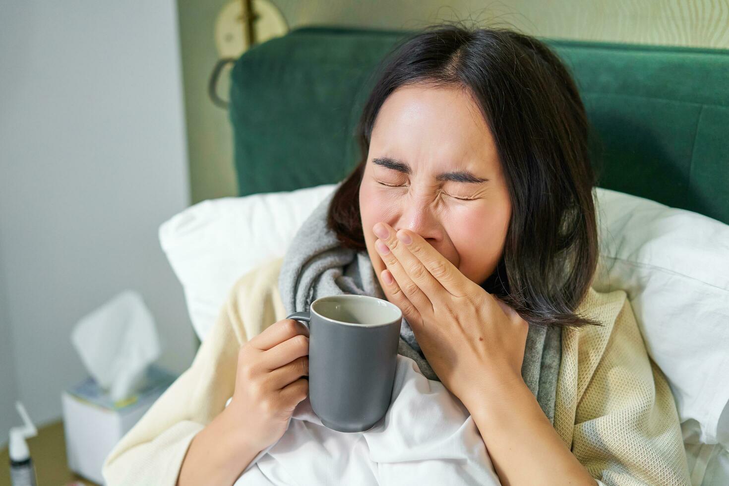 schließen oben von asiatisch Mädchen im Bett, Gefühl krank, fangen kalt und Niesen, abwischen flüssig Nase, Trinken heiß Tee foto