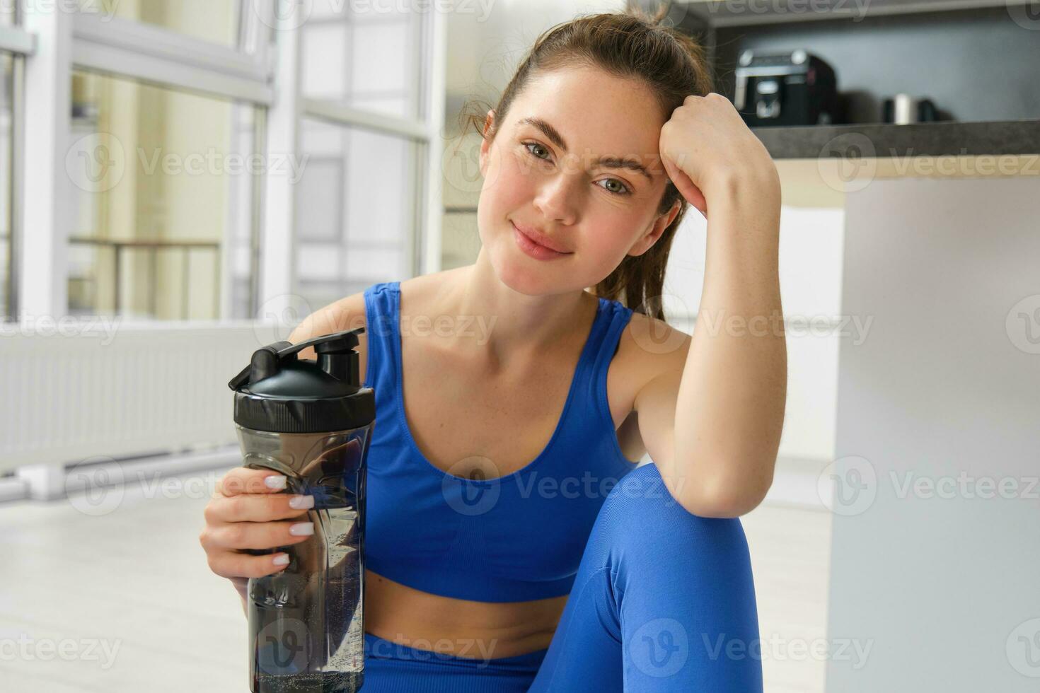 schön jung Sportlerin Getränke Wasser, bleibt hydratisiert während trainieren Ausbildung beim heim, tun Fitness Übungen im Leben Zimmer foto