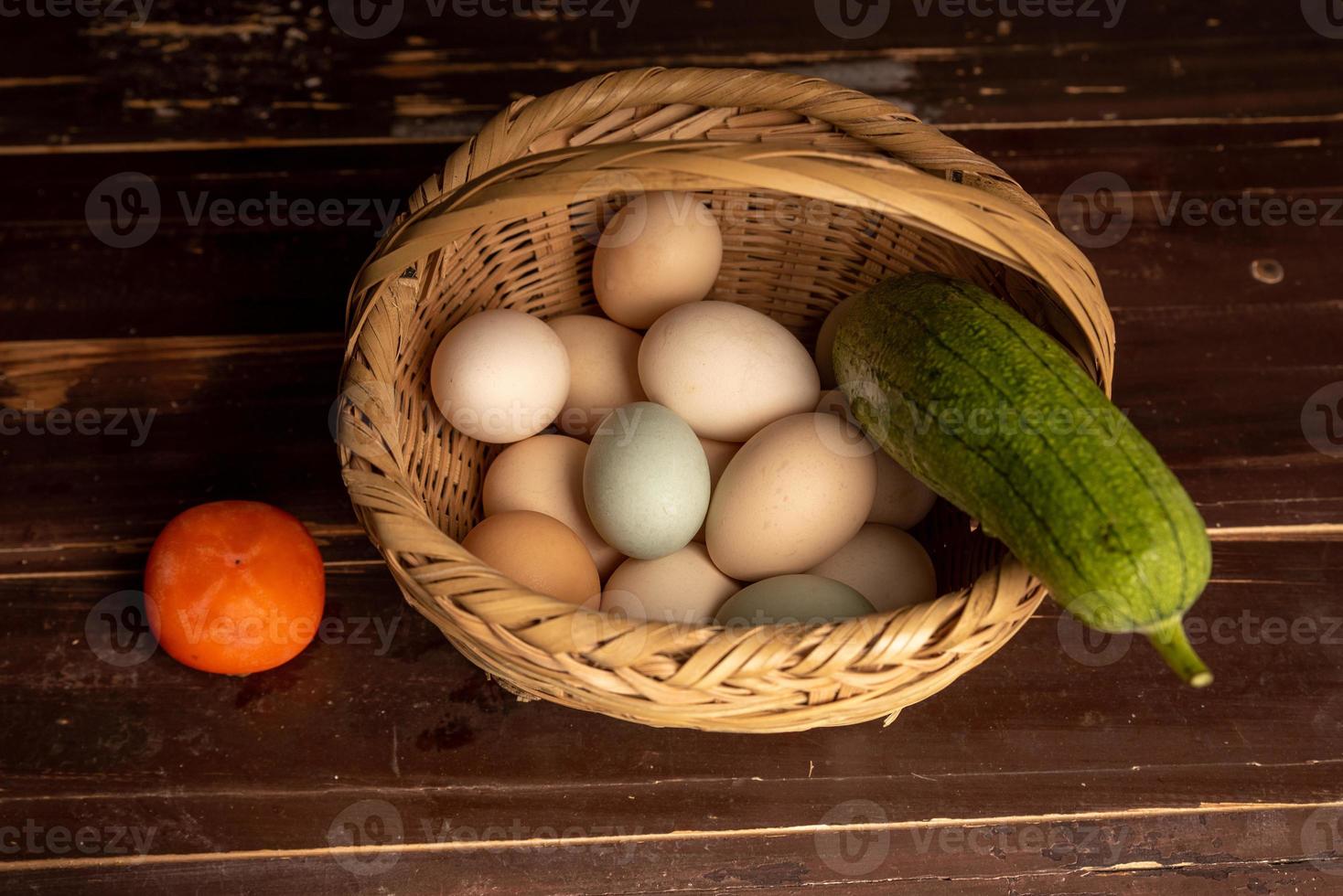 die Eier und anderes Obst und Gemüse im Korb liegen auf dem Holzmaserungstisch foto