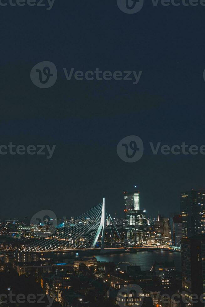 Nacht Antenne Aussicht von das schlaflos Stadt von Rotterdam und architektonisch Gebäude. glühend Wolkenkratzer und das berühmt Erasmusbrug Brücke. das modern Stadt von das Niederlande foto