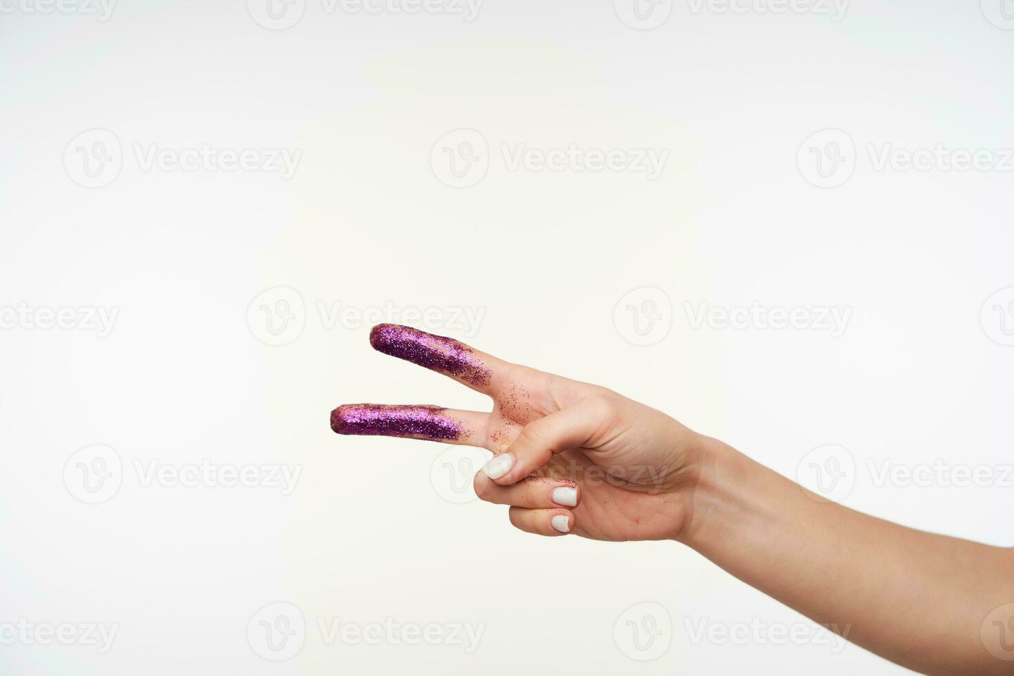 horizontal Schuss von hellhäutig Frau Hand mit violett funkeln Bildung mit Finger Frieden Geste während posieren Über Weiß Hintergrund. Körper Sprache Konzept foto