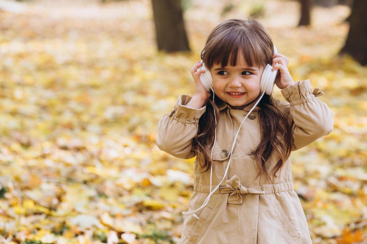 kleines Mädchen, das im Herbstpark Musik über Kopfhörer hört foto