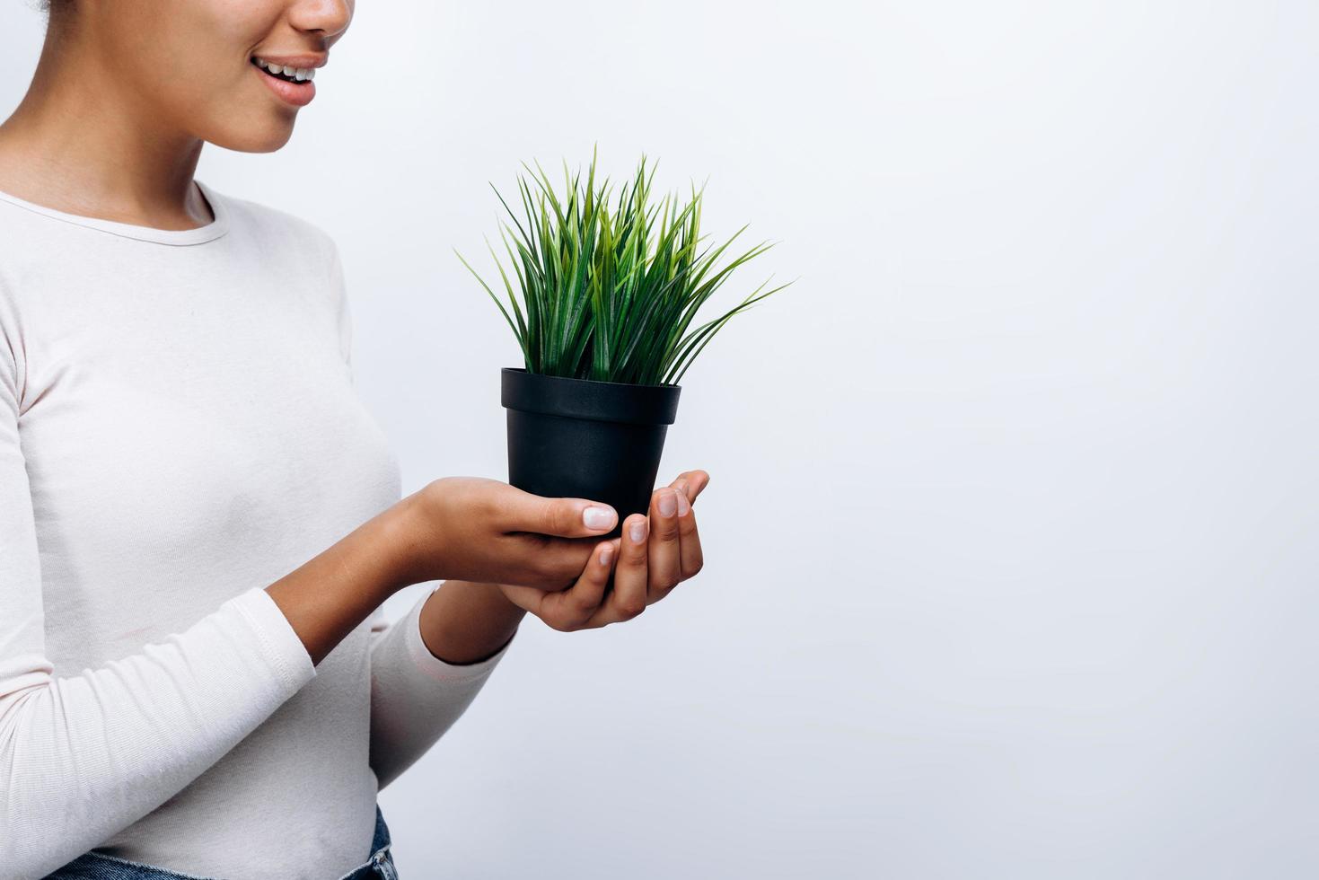 Seitenansicht, Mädchen, das einen schönen, grünen Blumentopf auf einem Hintergrund der weißen Wand hält, Platz für Text foto