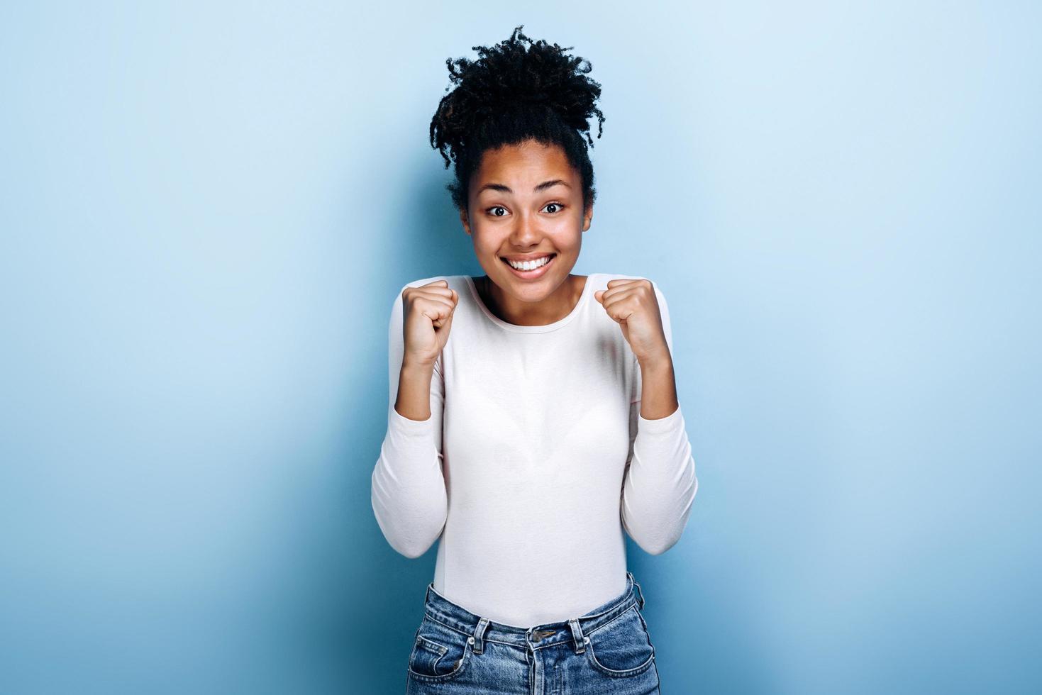 überglückliches afroamerikanisches tausendjähriges Mädchen, das auf blauem Studiohintergrund isoliert ist, Triumph gute Nachrichten erhalten. Gewinnerkonzept foto