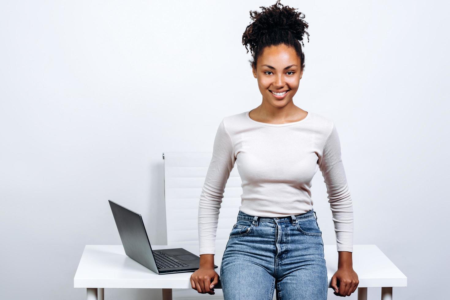 lächelnde, attraktive Geschäftsfrau auf dem Hintergrund eines Desktops in einem weißen Studio foto