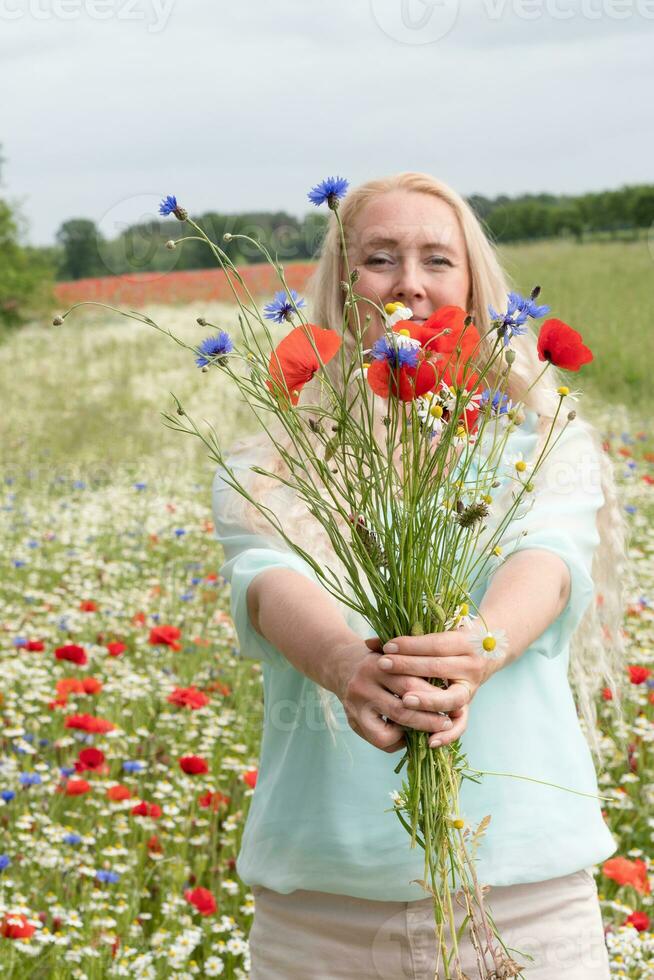 schön mittleren Alters blond Frau steht unter ein blühen Feld von Mohnblumen foto