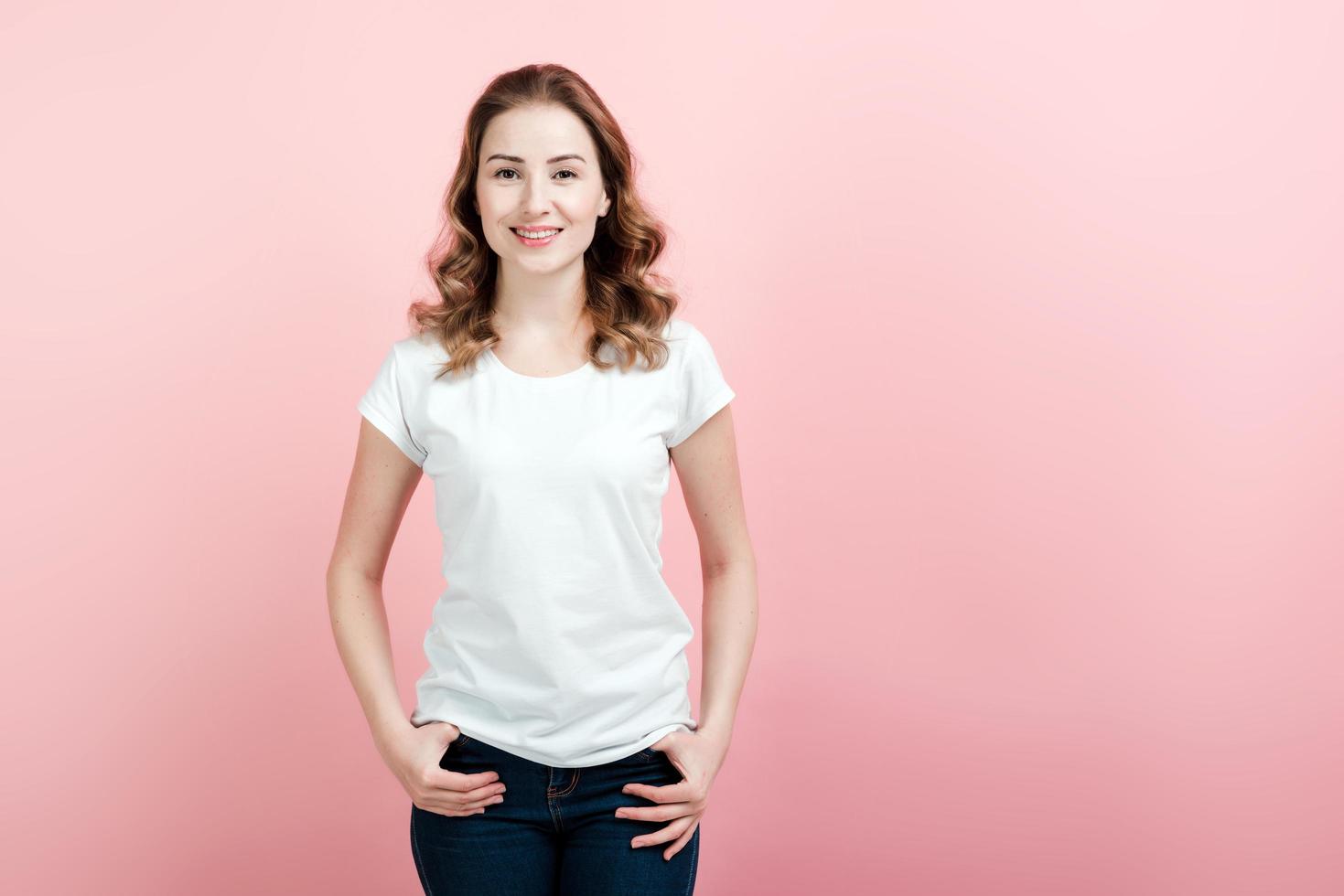 junge, schöne Frau in weißem T-Shirt und Jeans posiert auf rosa Wandhintergrund foto