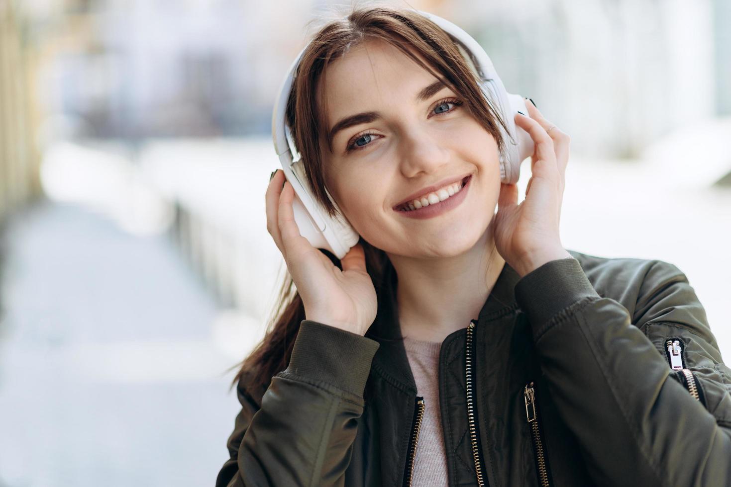 junge entzückende Frau mit süßem Lächeln mit Kopfhörern vor Stadthintergrund foto