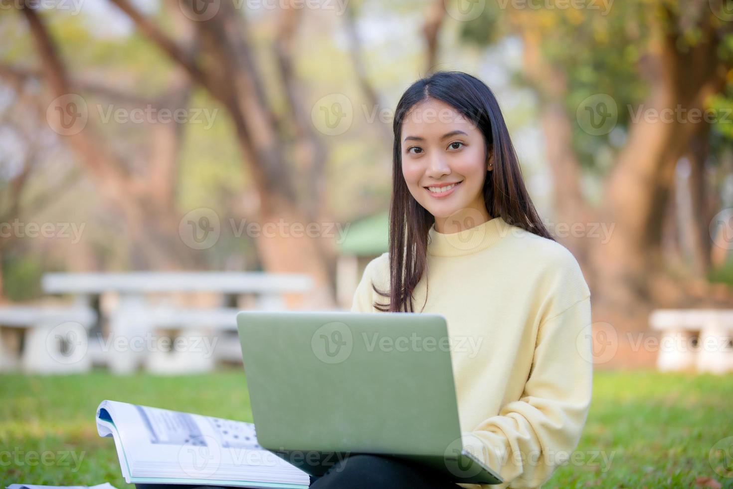 Asiatische Studentinnen lächeln und sitzen auf dem grünen Gras, arbeiten und lesen draußen zusammen in einem Park foto