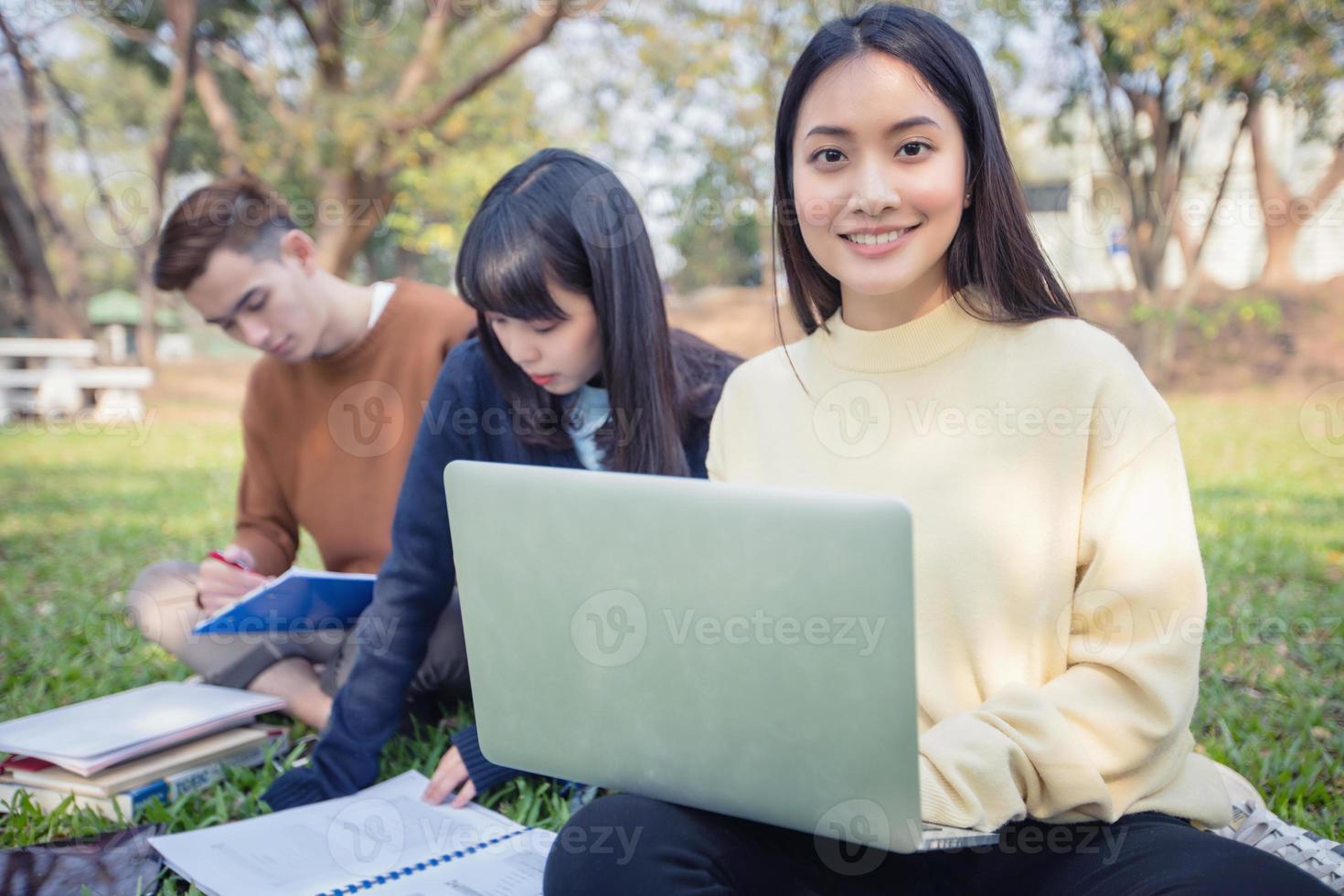 Gruppe von asiatischen Studenten, die auf dem grünen Gras sitzen und draußen in einem Park arbeiten und lesen? foto