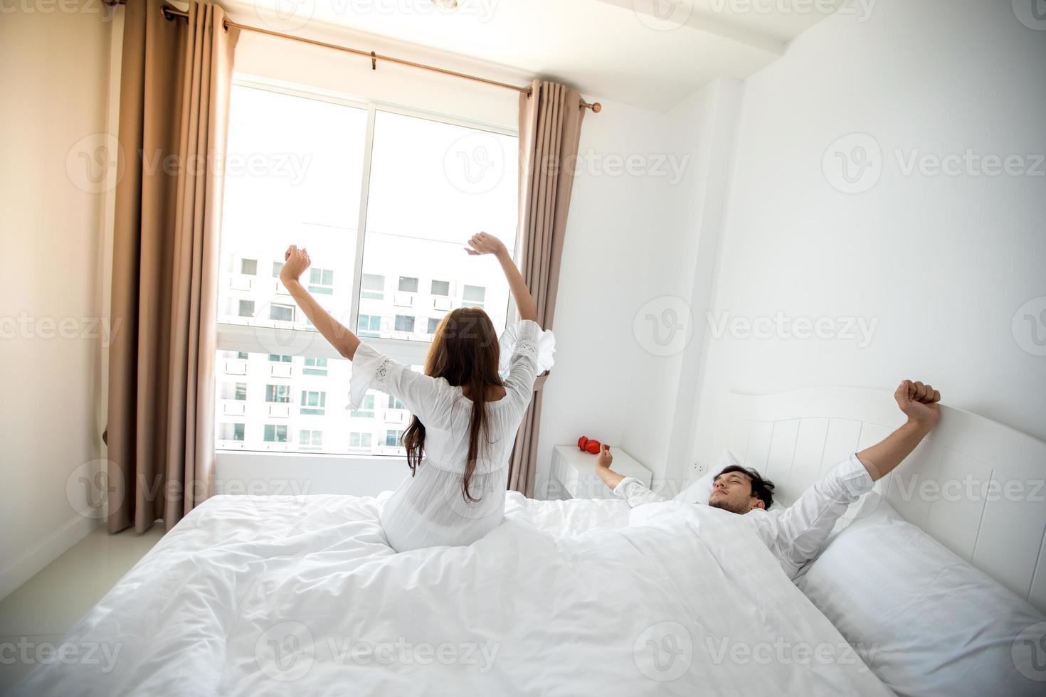 Liebespaare wachen ausgeruht in ihrem Bett auf und öffnen morgens die Vorhänge, um frische Luft zu schnappen. foto