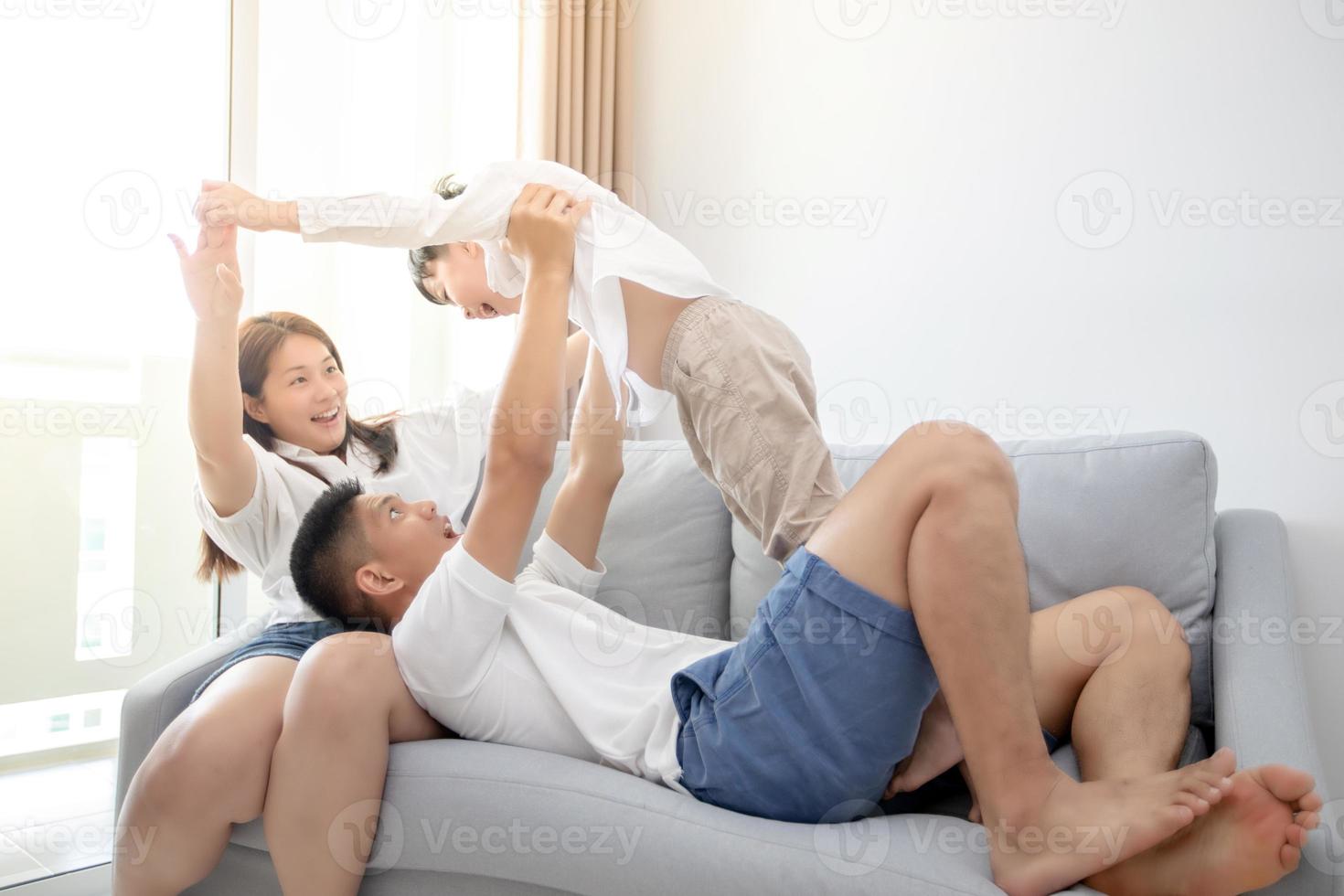 glückliche asiatische familie mit sohn zu hause auf dem sofa, der spielt und lacht foto