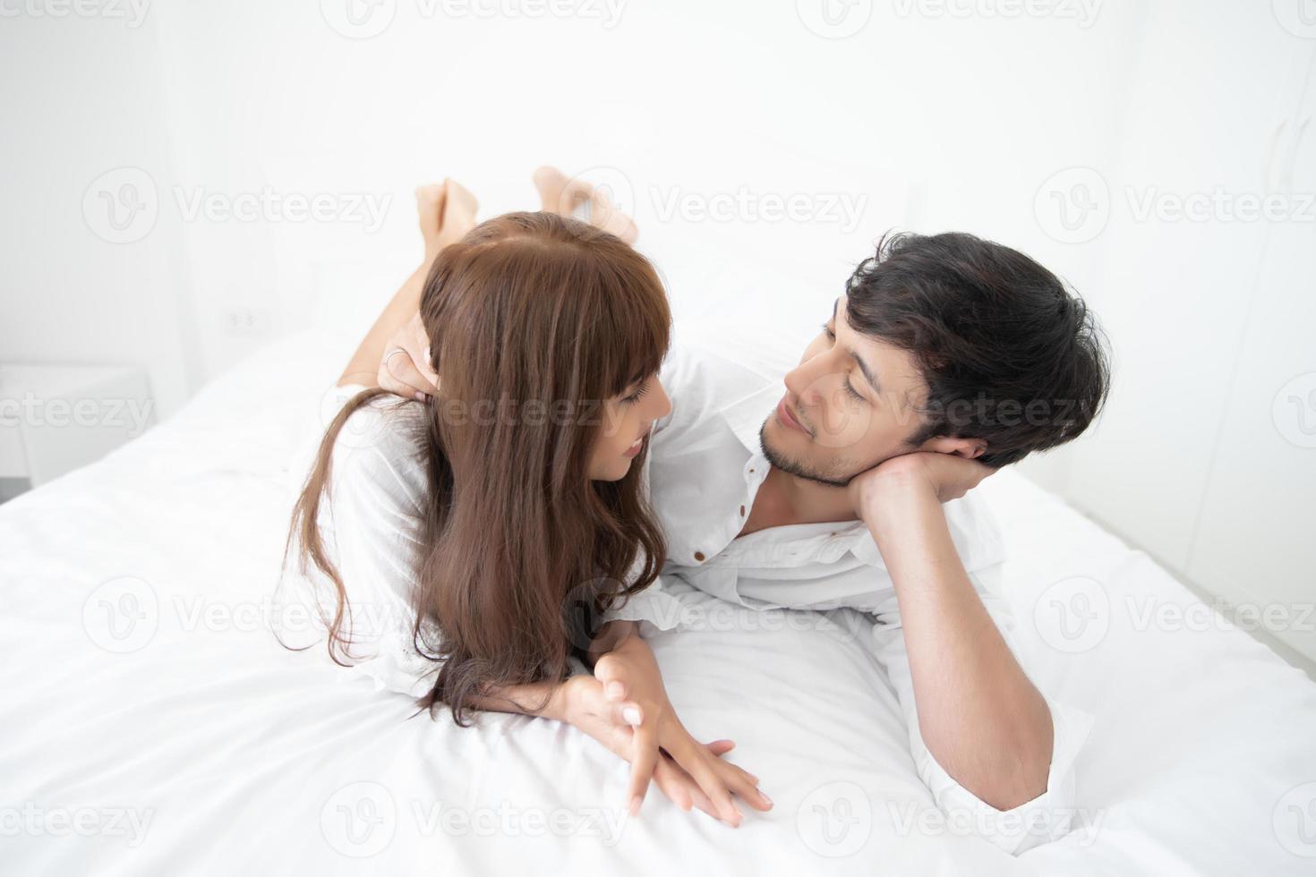 Paarliebhaber, der auf dem Bett Glückslebensstil legt und lächelndes Mädchen im weißen Bett entspannt foto