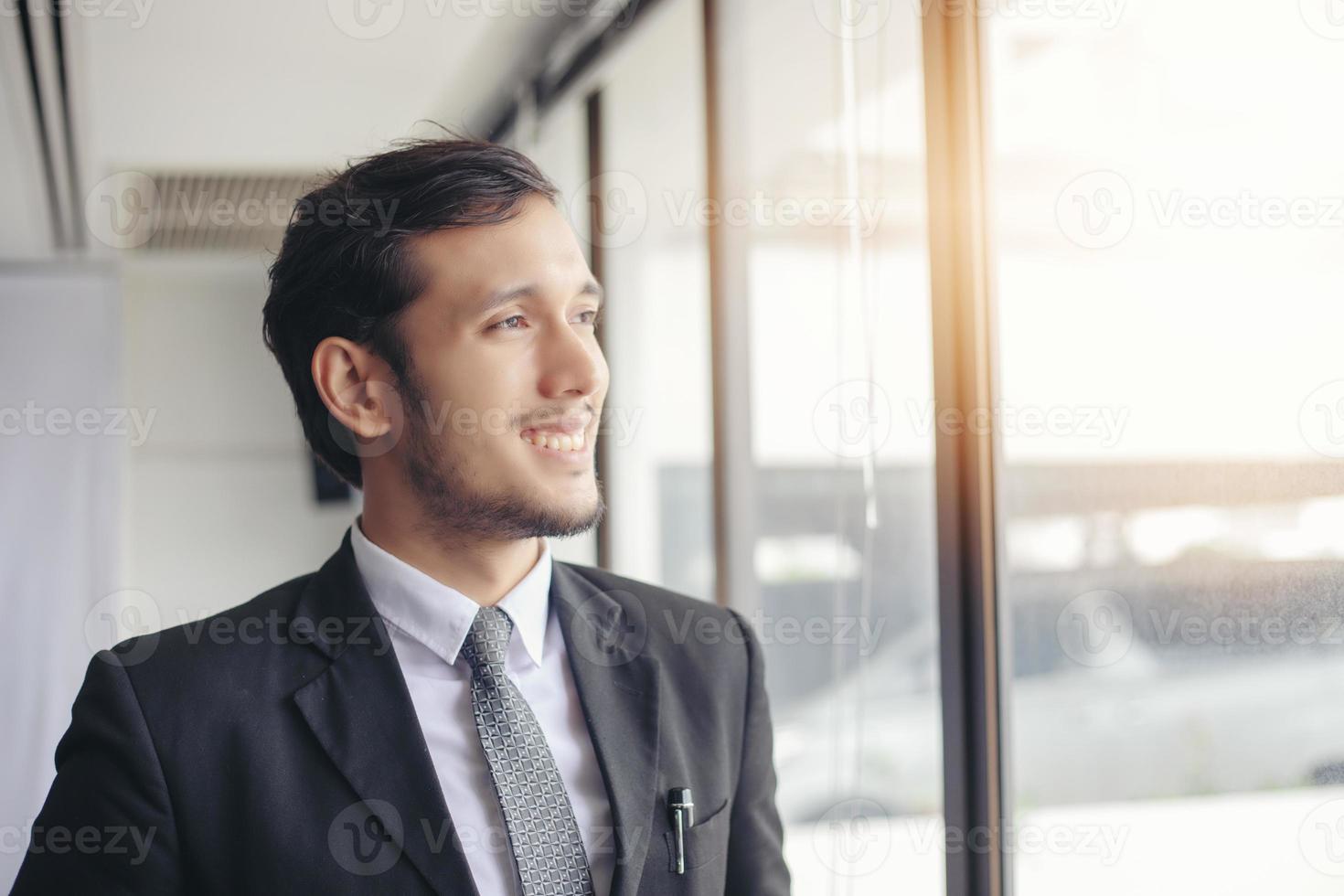 glücklicher gutaussehender Geschäftsmann, der im Büro steht und lächelt foto