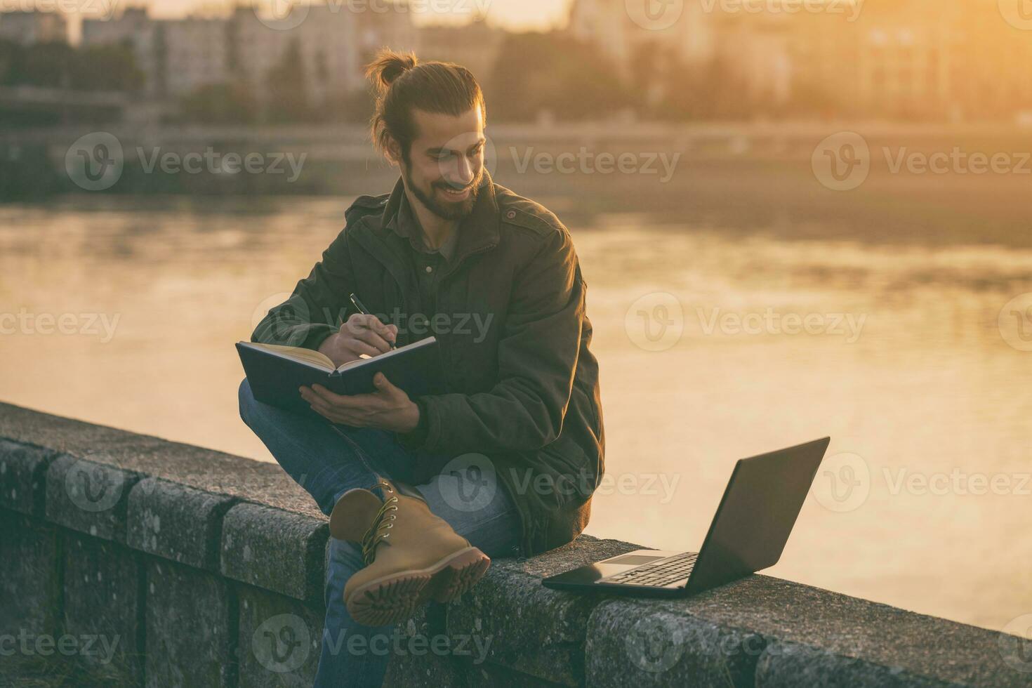 gut aussehend Geschäftsmann mit persönlich Veranstalter und Laptop während Sitzung durch das Fluss.getönt Bild foto