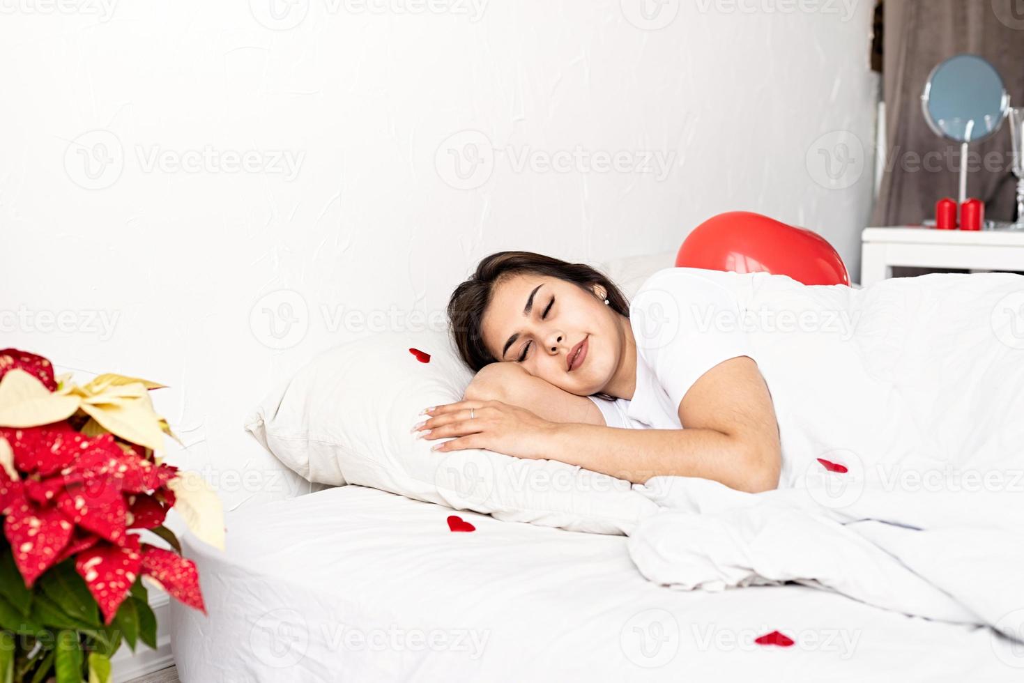 junge brünette frau, die im bett mit roten herzförmigen luftballons und dekorationen schläft foto