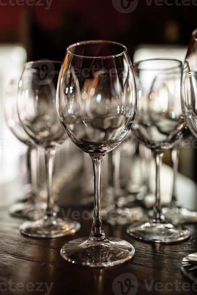 leere Weingläser. schöne neue gläser für wein aus glas stehen in gleichmäßigen reihen auf einem holztisch in einem restaurant. selektiver Fokus foto