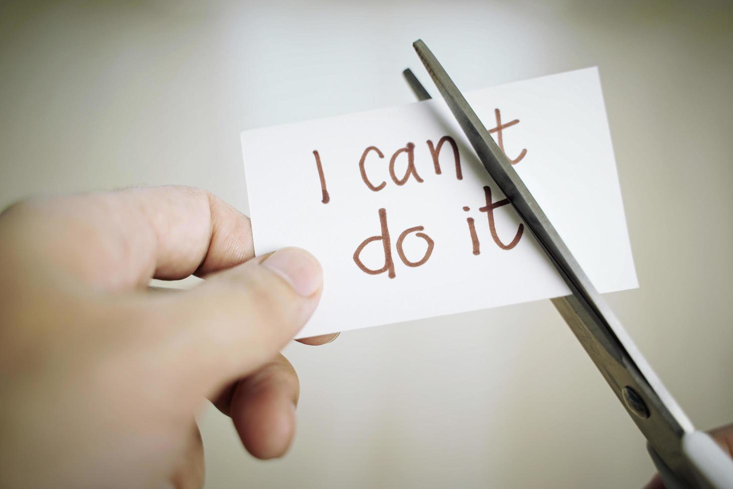 Mann Hand schneidet Papiernotiz mit einer Schere, um t-Wort aus Texten zu entfernen, die ich nicht tun kann. positive Einstellung, Selbstvertrauen und Motivationskonzept foto