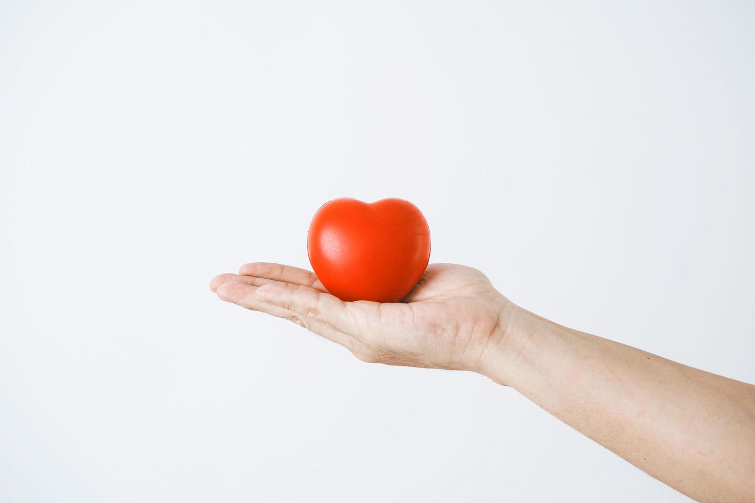 die Hand eines Mannes, der ein rotes Herz auf weißem Hintergrund hält foto