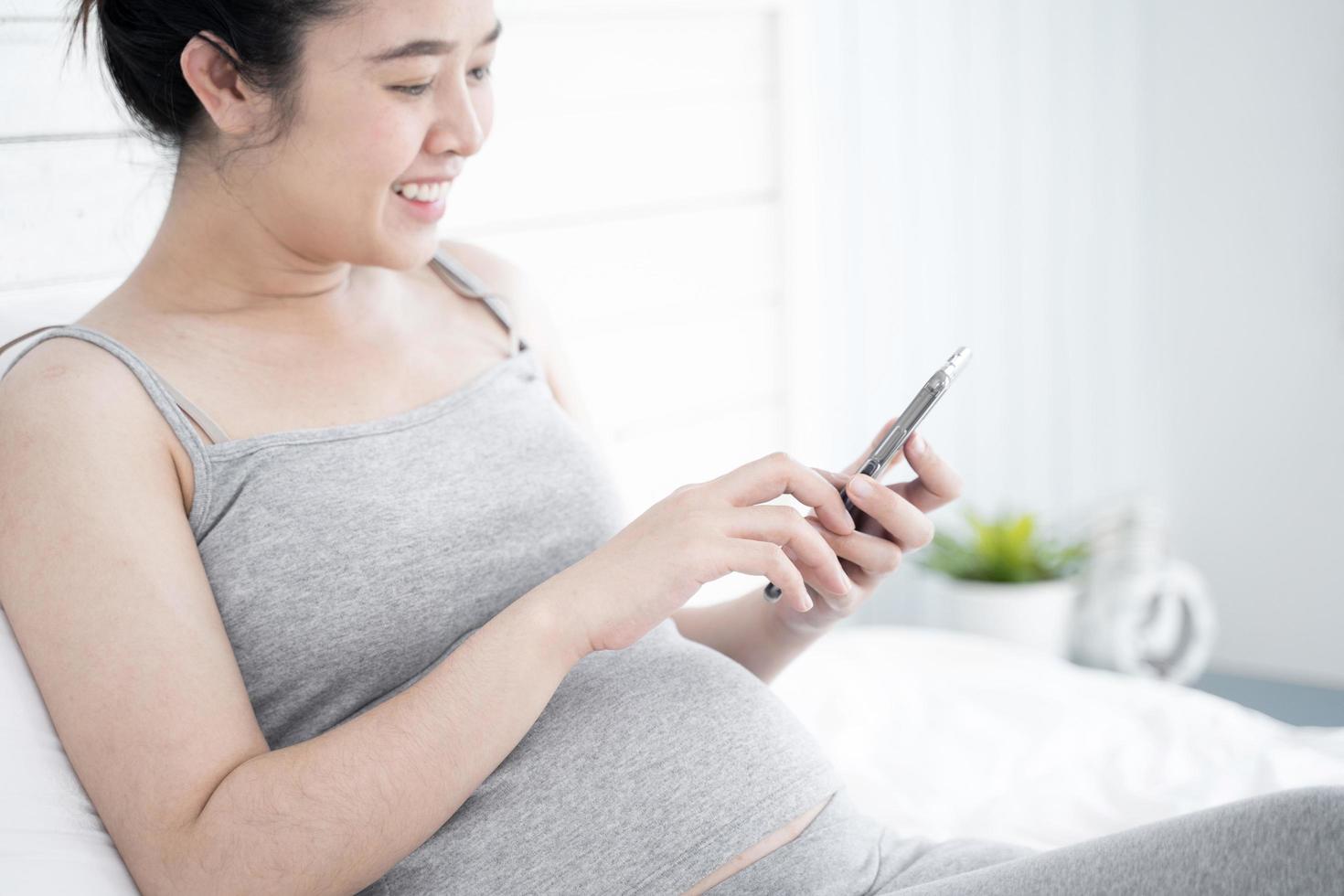 schöne schwangere Frau mit Handy in ihrem Schlafzimmer foto