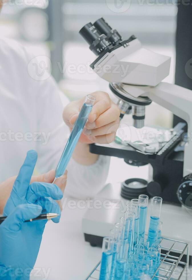 Wissenschaftler oder medizinisch im Labor Mantel Arbeiten im biotechnologische Labor, Mikroskop Ausrüstung zum Forschung mit Mischen Reagenzien im Glas Flasche im klinisch Labor. foto