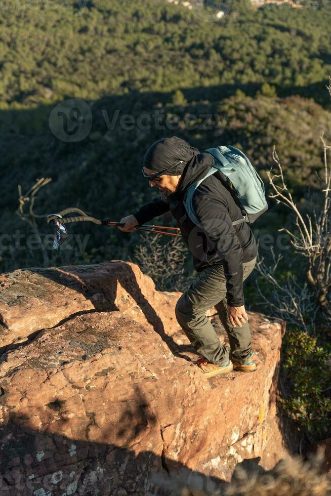 mittleren Alters Mann klettert das Berg im das garraf natürlich Park, unterstützt durch Wandern Stangen. foto
