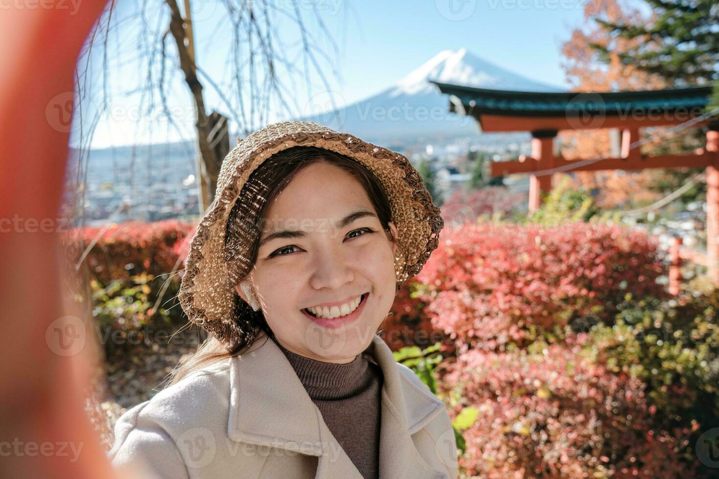 heiter asiatisch weiblich Tourist tragen ein Hut nimmt ein Selfie im das Hintergrund im Japan foto