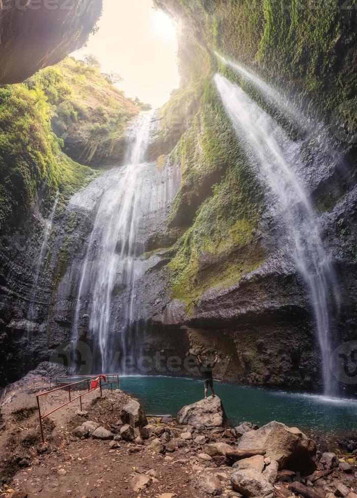 Mann ist glücklich auf Felsen im Madakaripura Wasserfall im tropischen Regenwald foto