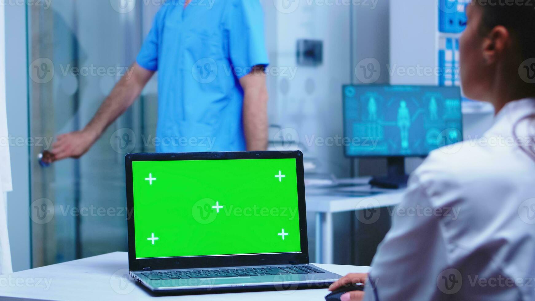 Chroma Schlüssel auf Laptop im medizinisch Klinik benutzt durch Arzt tragen Weiß Mantel und Krankenschwester mit Blau Uniform Öffnung Kabinett Glas Tür. Medizin tragen Uniform mit Notizbuch mit Kopieren Raum auf Anzeige im medizinisch Klinik. foto