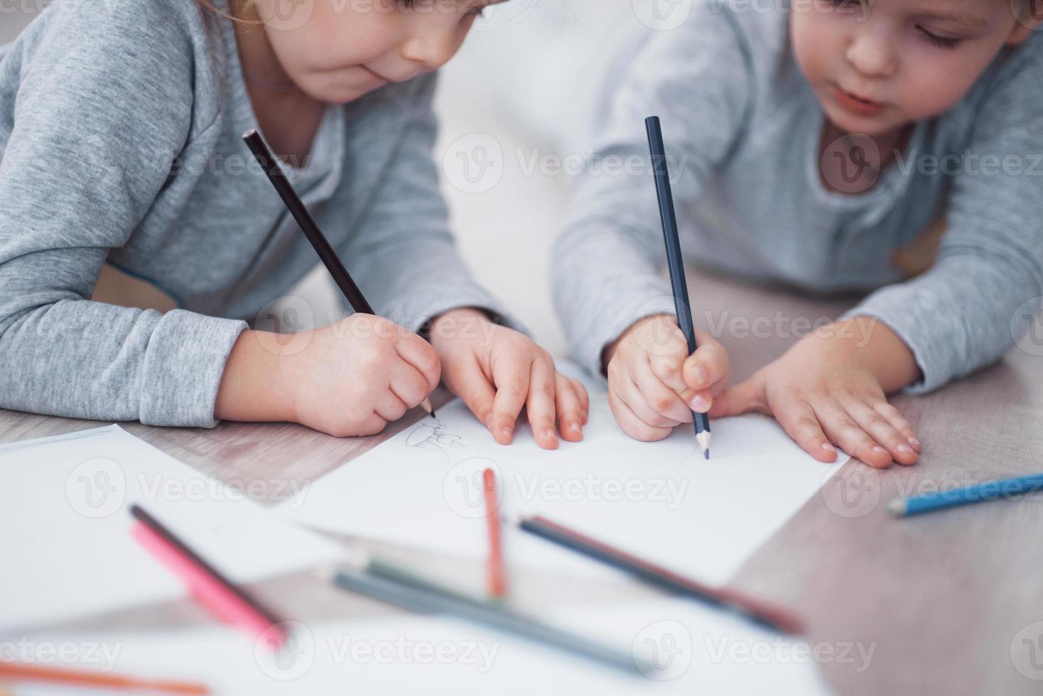 Kinder liegen im Schlafanzug auf dem Boden und zeichnen mit Bleistiften. süße Kindermalerei von Bleistiften. Hand von Kindermädchen und -jungen zeichnen und malen mit Buntstift. Nahaufnahme foto