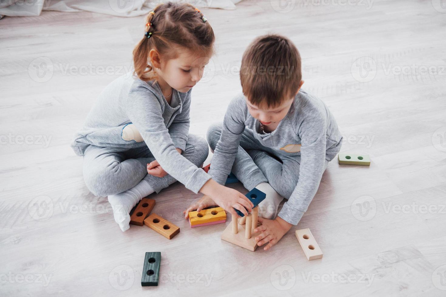 Kinder spielen mit einem Spielzeugdesigner auf dem Boden des Kinderzimmers. zwei Kinder spielen mit bunten Blöcken. Lernspiele im Kindergarten foto