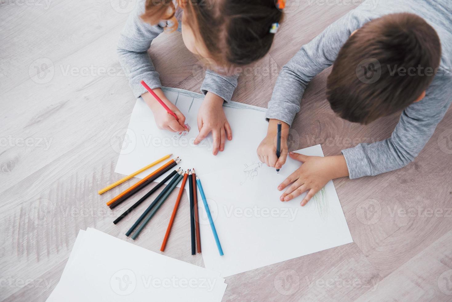 Kinder liegen im Schlafanzug auf dem Boden und zeichnen mit Bleistiften. süßes Kind malen mit Bleistiften foto