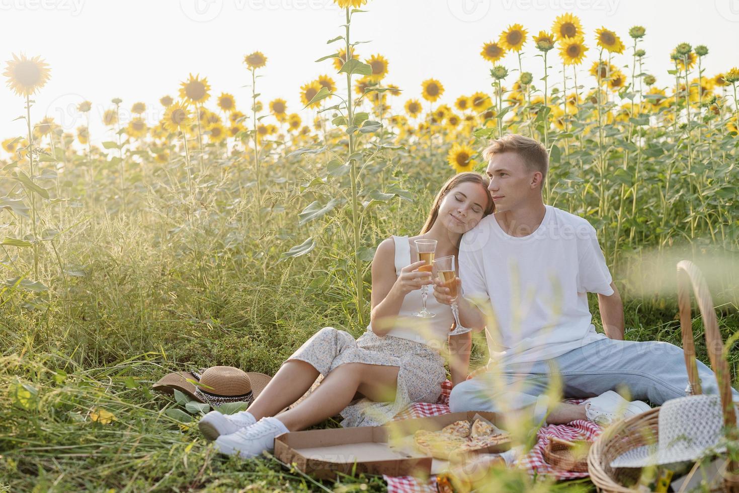 junges Paar beim Picknick auf Sonnenblumenfeld bei Sonnenuntergang foto