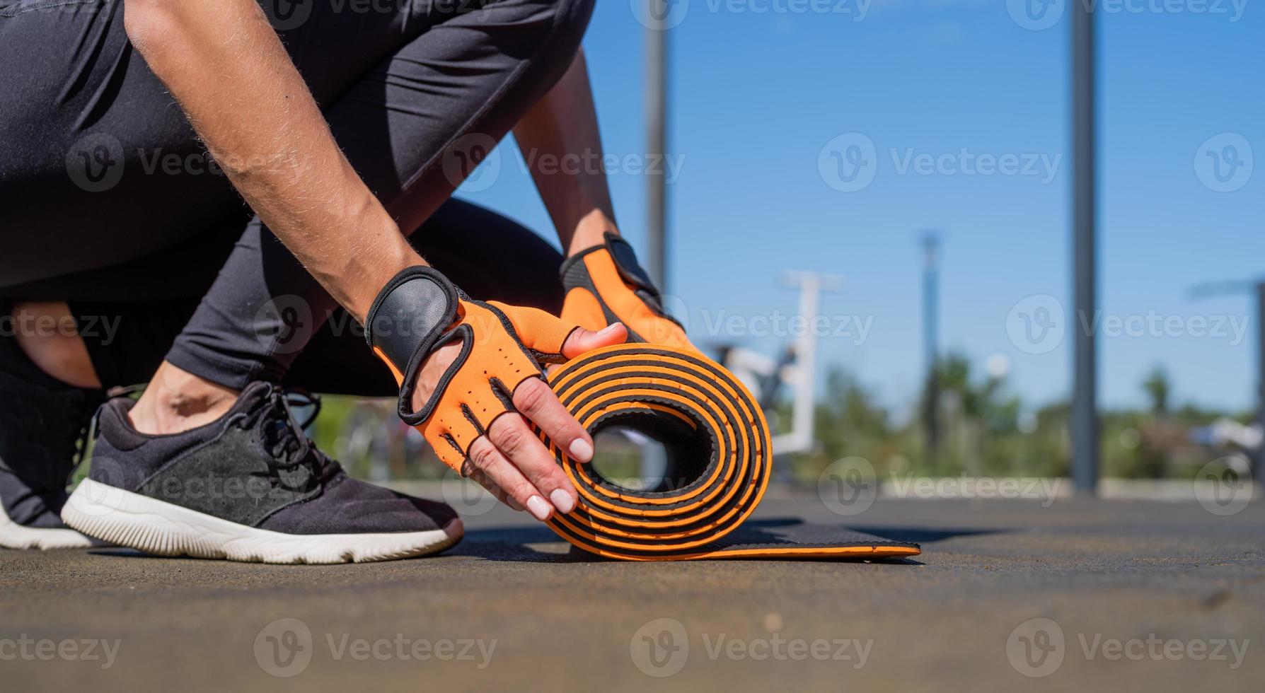 Nahaufnahme von Frauenhänden in Sporthandschuhen, die Fitnessmatten rollen, die sich auf das Training vorbereiten foto