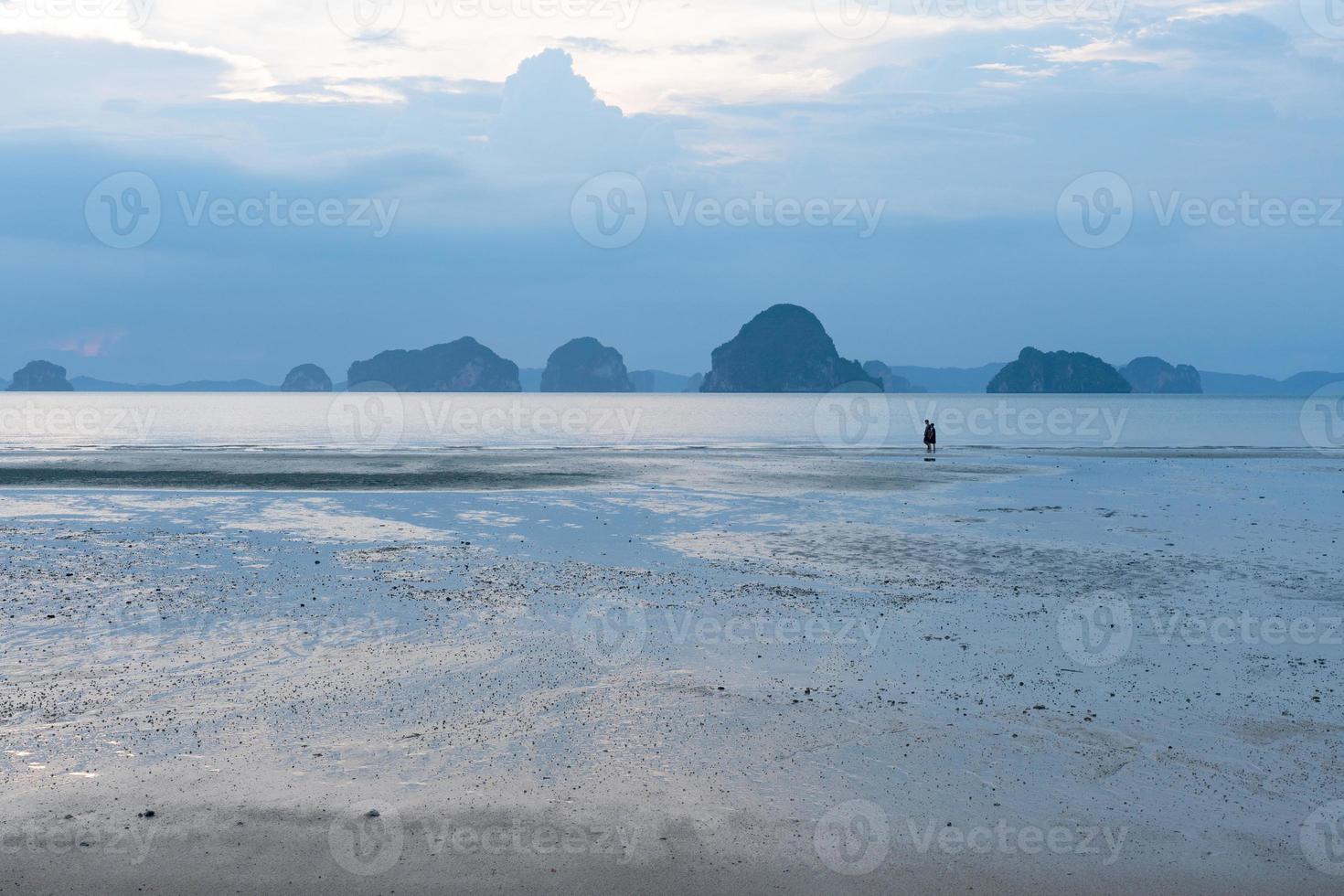 Landschaft des schönen Ozeans und des Strandes bei Sonnenuntergang mit Paaren, die als Hintergrund gehen foto