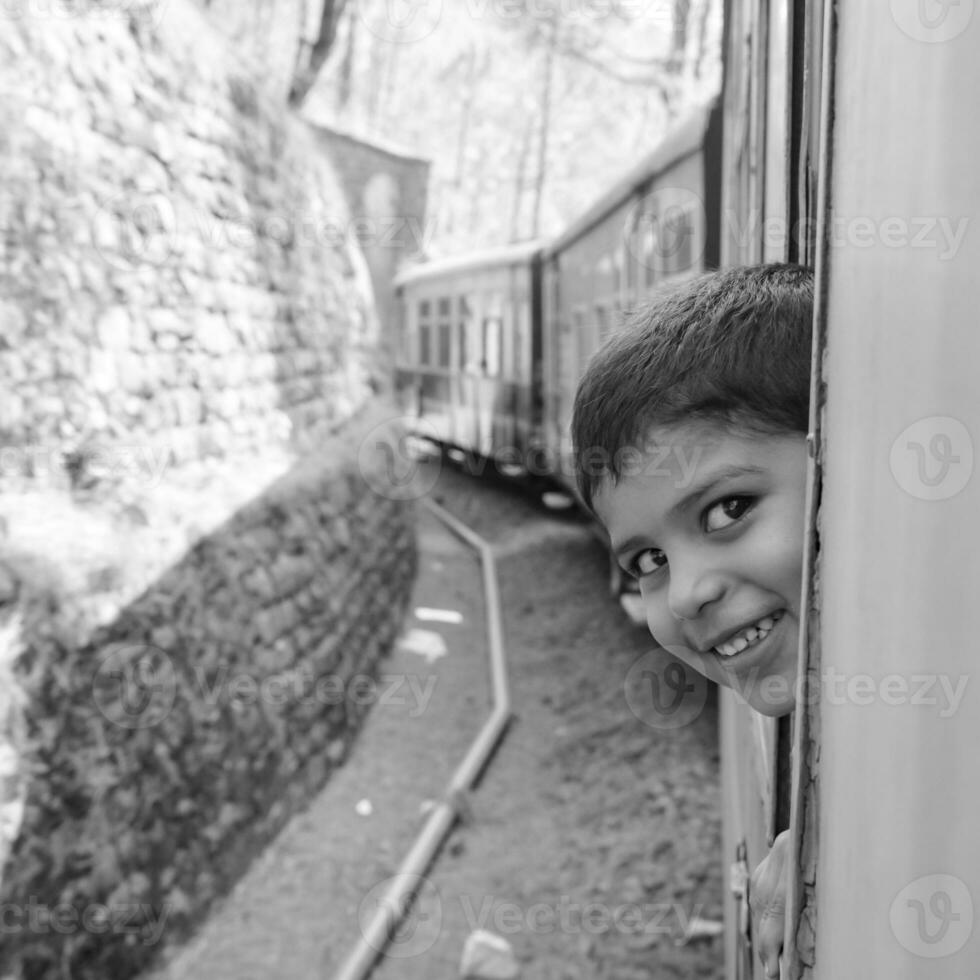 wenig Junge Reisen im Spielzeug Zug ziehen um auf Berg Steigungen, schön Sicht, einer Seite Berg, einer Seite Senke ziehen um auf Eisenbahn zu das hügel, unter Grün natürlich Wald. Spielzeug Zug shimla foto