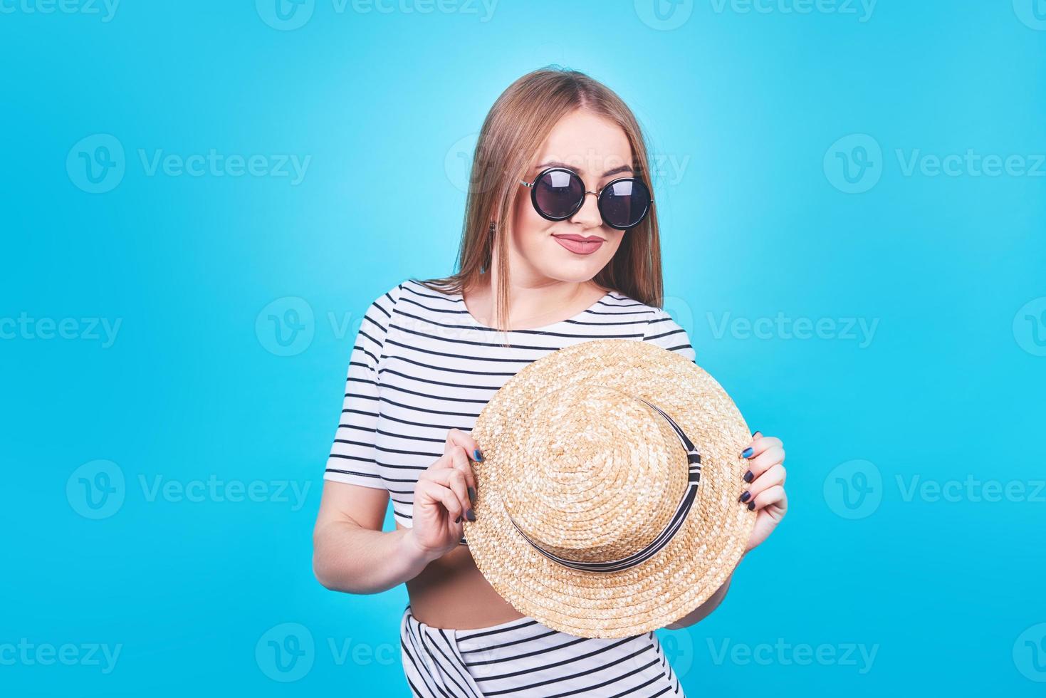 attraktives mädchen in weißen und schwarzen streifen, hut, sonnenbrille, emotional geöffneter mund auf hellblauem hintergrund mit perfektem körper. isoliert. Studioaufnahme foto